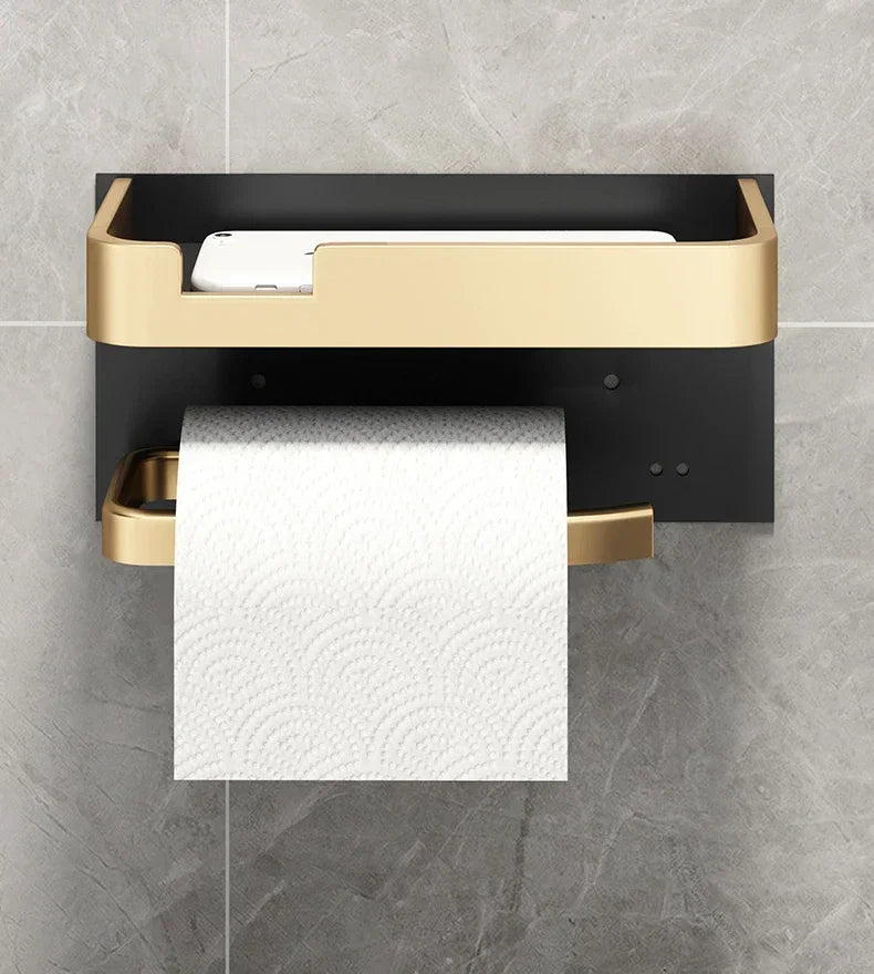 Black Gold toilet paper holder from MC THE BLACK DIAMOND, mounted on bathroom wall with a roll of toilet paper.