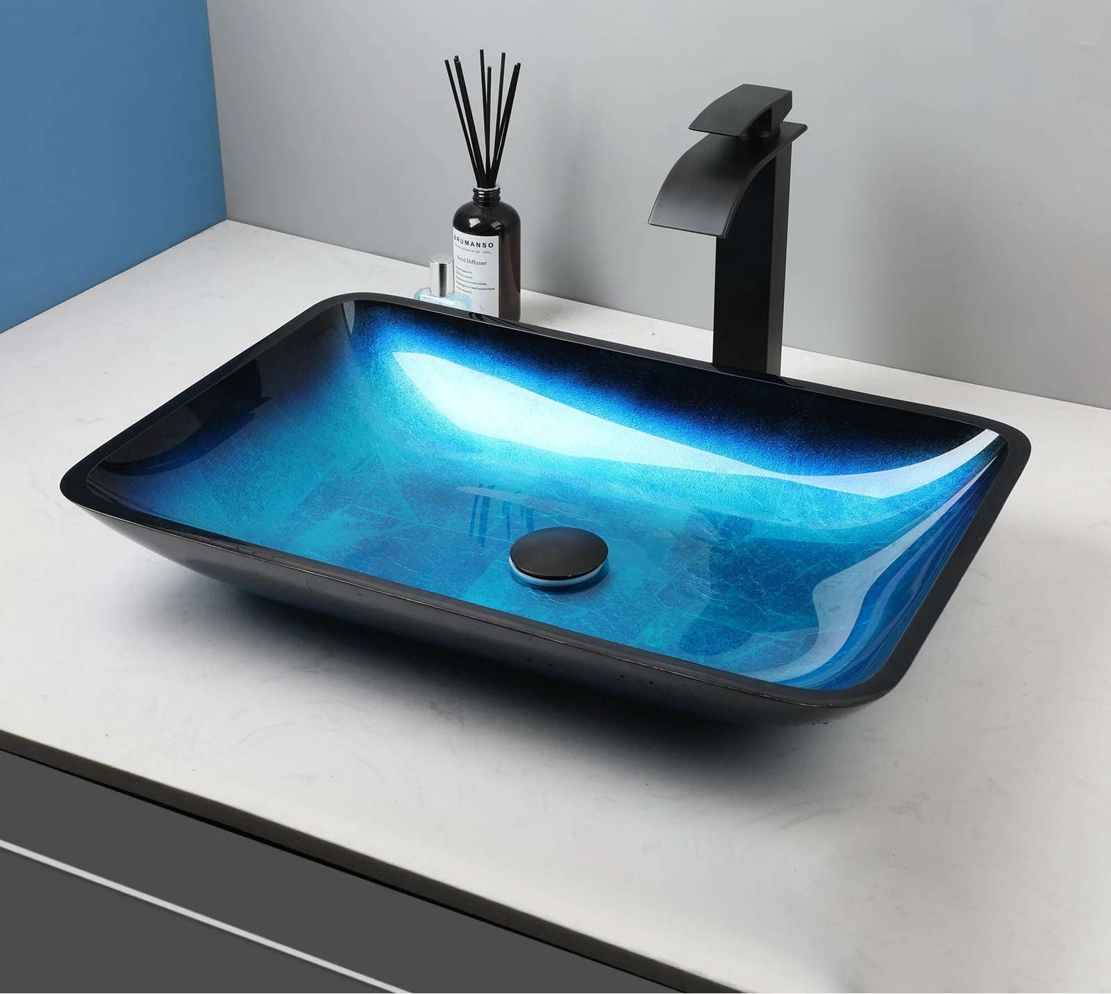 Black vessel sink with tempered glass basin and blue oval design paired with a black waterfall faucet in a modern bathroom setting.